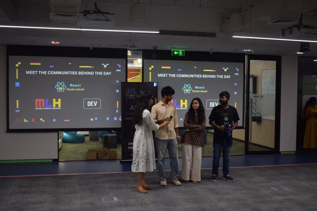The Gitora team on stage in front of screens reading Meet the Communities Behind the Day, with React Hyderabad, MLH, and DEV